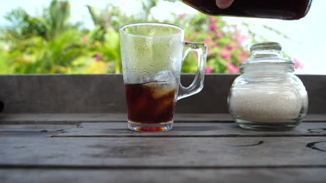 Close-up-of-person-refilling-their-iced-beverage-on-outdoor-patio-with-tropical-background