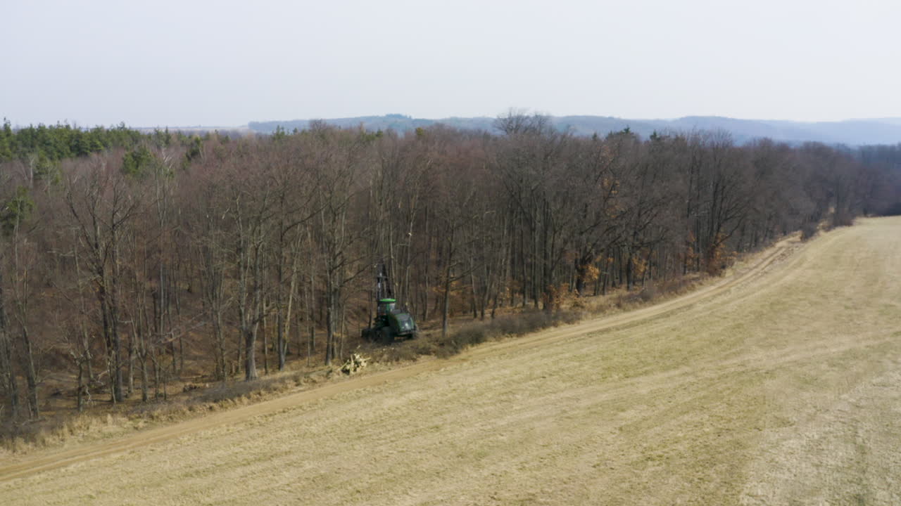 죽은 잎이 없는 숲 가장자리에 있는 임업 수확기 차량, 드론 샷