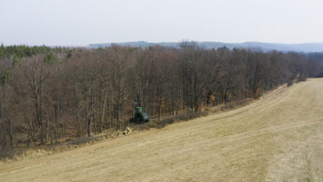 forestry harvester vehicle on edge of dead leafless forest, drone shot