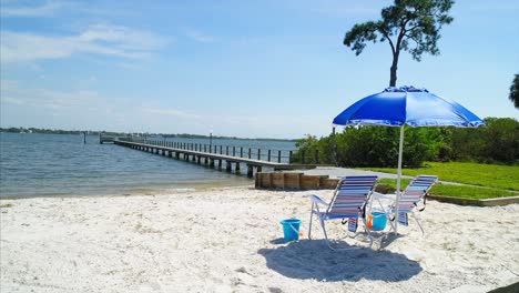 beach chairs and umbrella on a beach next to a pier by a water vista