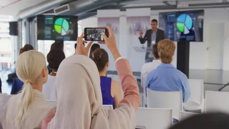 woman in audience at a business conference filming with smartphone