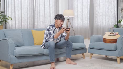 집에서 스마트폰으로 게임을 하는 젊은 남자