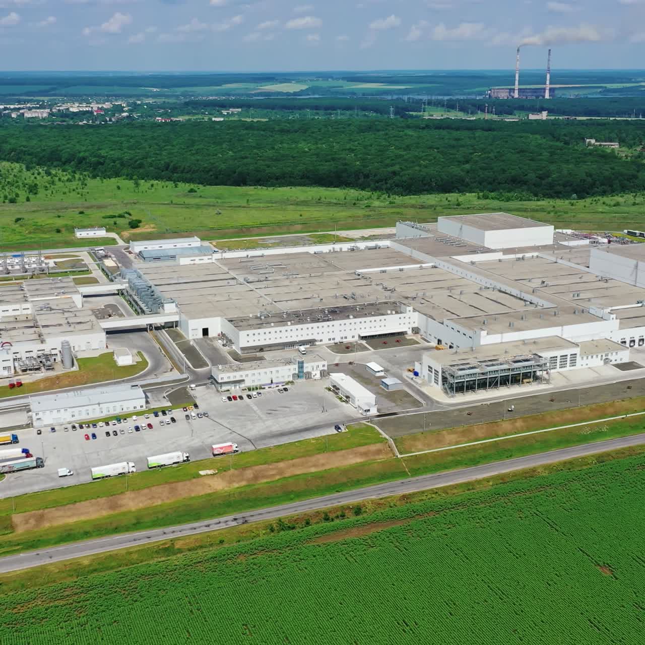 Modern factory in the countryside. Huge industrial complex among picturesque green fields. New manufacture among nature. Aerial view.
