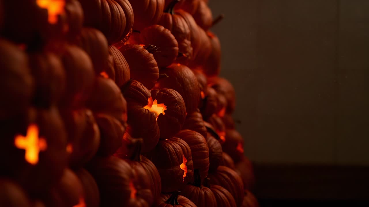 Camera opening close-up, panning stacked carved pumpkins in dim hallway, flickering LEDs