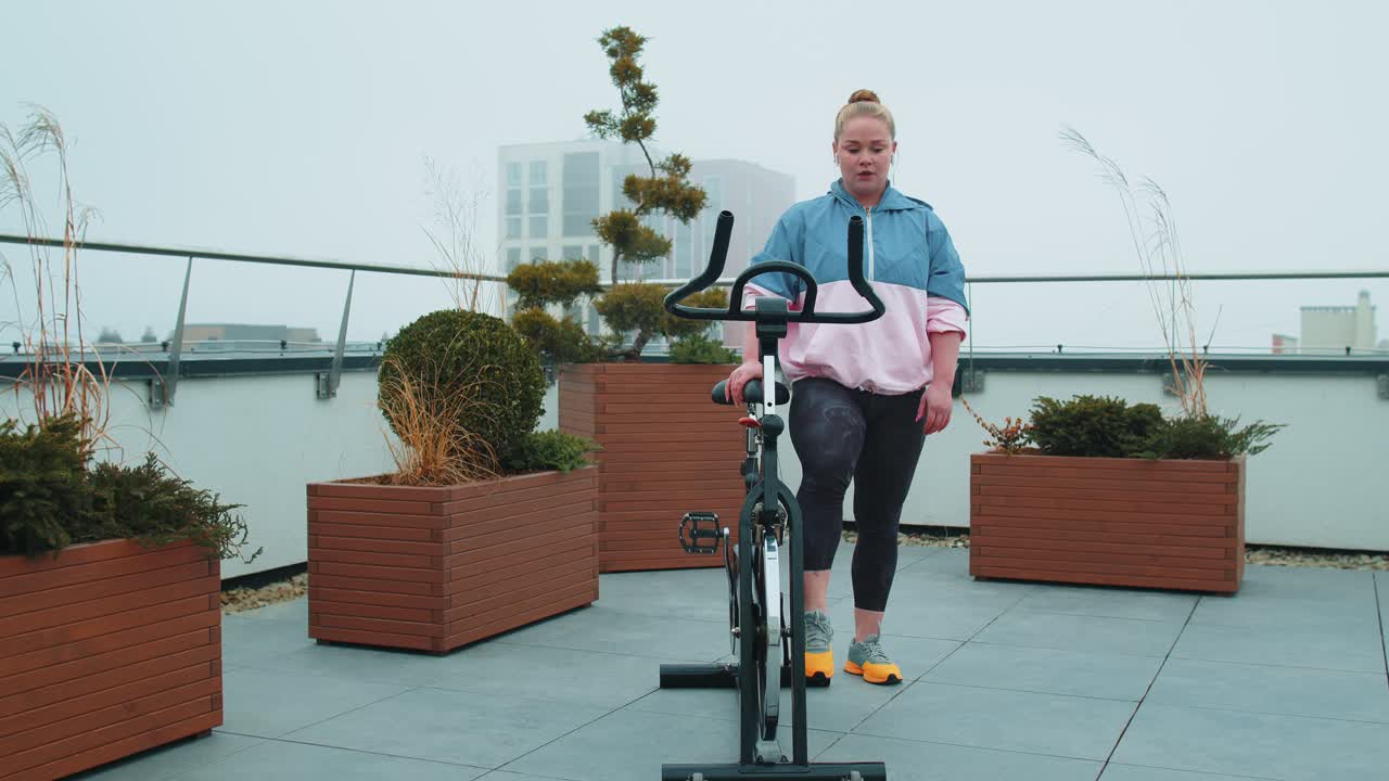 Athletic woman riding on spinning stationary bike training routine on house rooftop weight loss