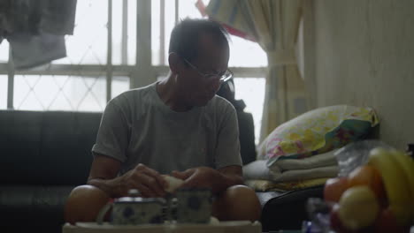 an old chinese man eating lunch in the living room of a cramped apartment