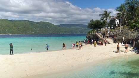 tourists relax on the white sandy beach with crystal clear water and lush mountains in the background