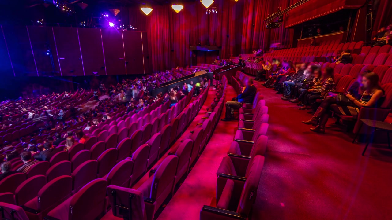 Tilskuere samles i auditoriet og ser forestillingen i teateret timelapse. Stor sal med røde lenestolseter. Publikum fyller plassene til lyset slås av. Sett fra høyre side.