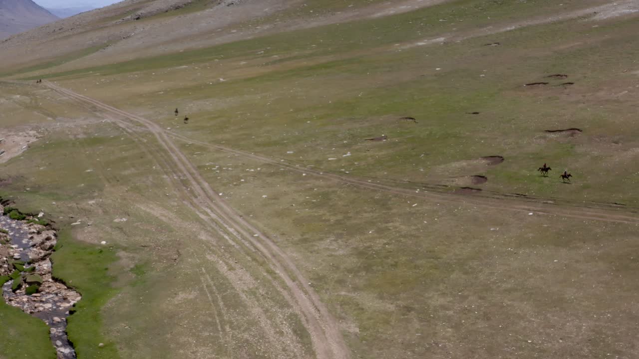 jinetes nómadas tradicionales de mongolia, a caballo en un paisaje de valle verde, idílico prado mongol con un pequeño arroyo de río, toma de visión general de un avión no tripulado