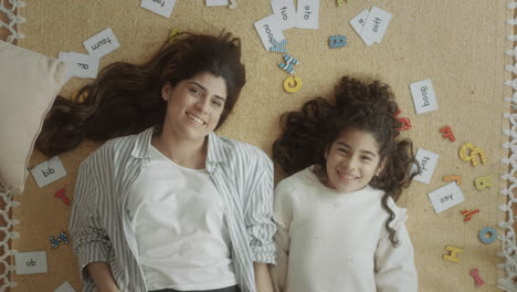 joyous girl and mother lying among letters and word cards