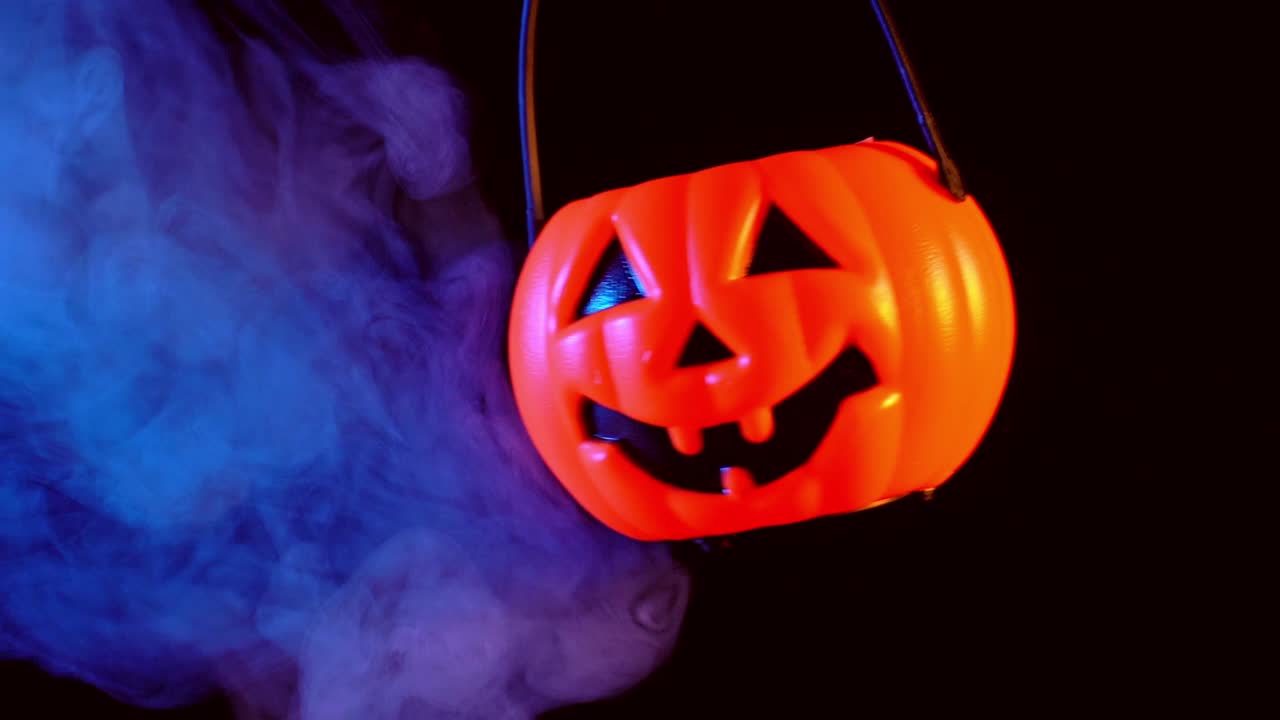 concepto de halloween - moviendo linterna de calabaza de plástico con humo azul-naranja alrededor aislado en fondo negro oscuro, aterrador y estado de ánimo de horror.