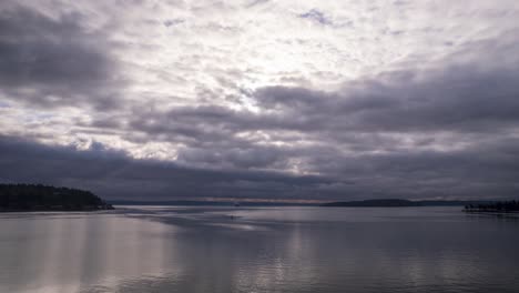 low dark marine layer clouds reflect off the calm still water, aerial hyperlapse