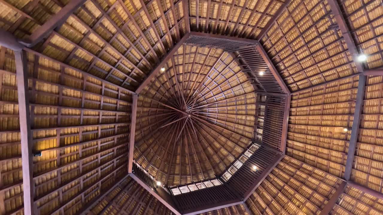 Camera rotates beneath an octagonal bamboo roof, highlighting intricate wooden structure and warm ambient lighting in a tropical indoor setting