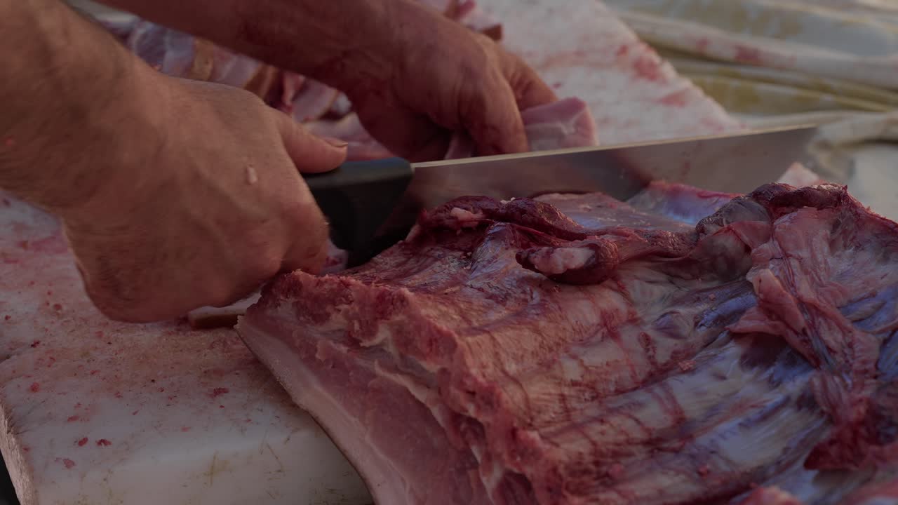 hands cut raw rib section of pig with heavy knife on white board