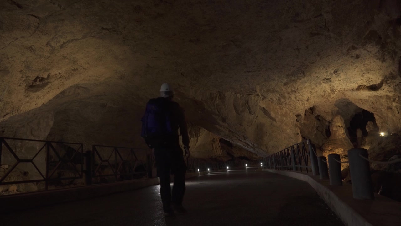Uomo che cammina attraverso le Grotte di San Giovanni in Sardegna, Italia, mostrando il passaggio della grotta calcarea, le formazioni rocciose e il paesaggio sotterraneo naturale