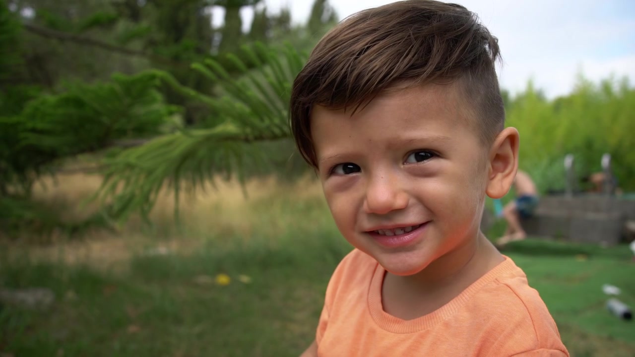 Un niño sonríe mientras mira directamente a la cámara al aire libre, retrato de primer plano