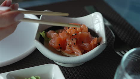 a woman with chopsticks in hand takes a piece of salmon tartare with sesame and herbs