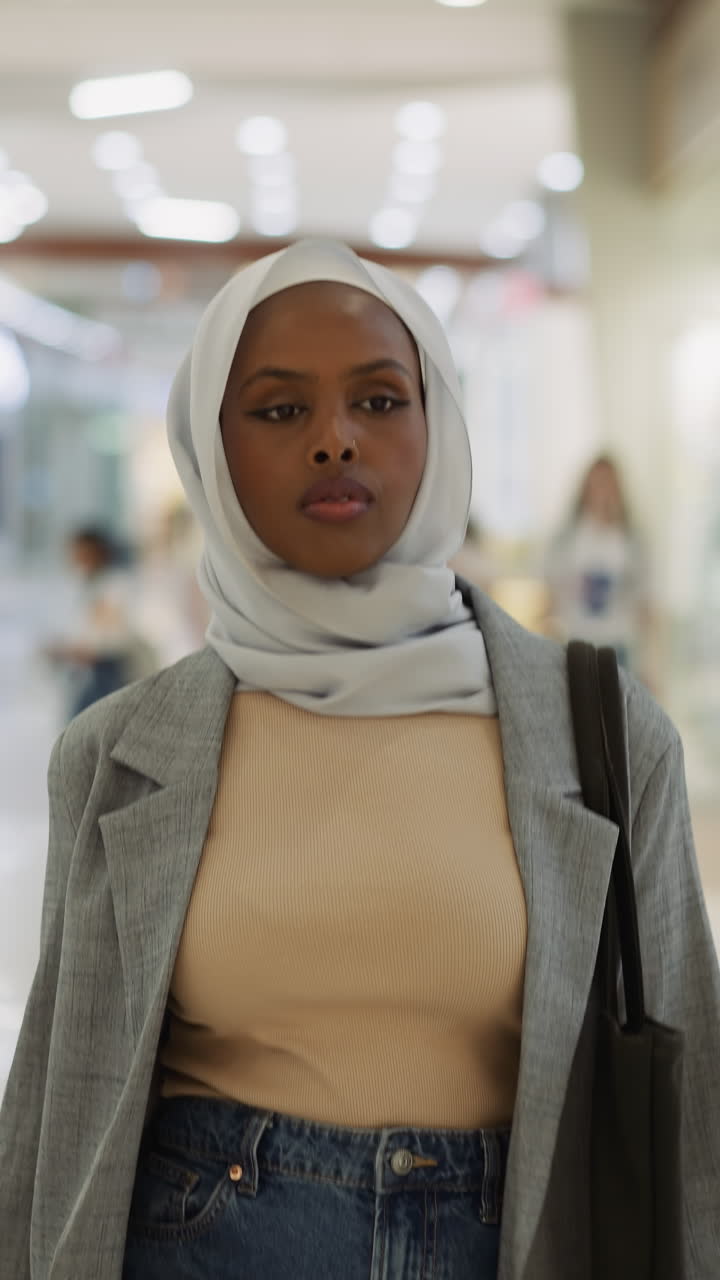 Confident African-American woman with chiffon hijab walks along hallway gallery in trade mall slow motion. Muslim lady visits shopping center