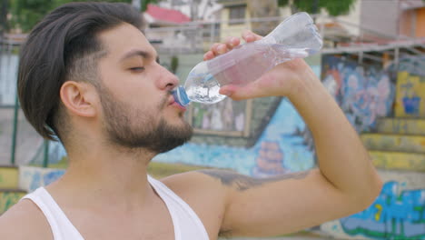 chico guapo bebiendo agua fresca de una botella de plástico en un parque de patinaje