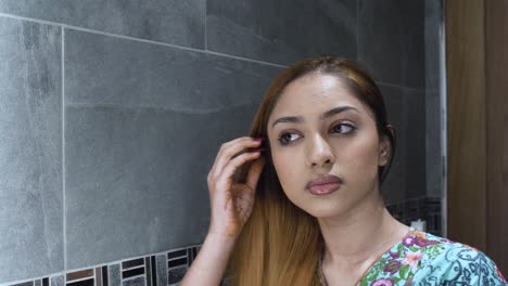 Close-Up-of-Young-Asian-Indian-female-combing-her-hair-in-mirror-in-bathroom