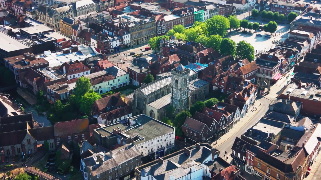 Droneudsigt over St Thomas Kirke i det centrale Salisbury, der viser dens historiske tårn, omkringliggende hustage, gader og den nærliggende markedsplads i Wiltshire