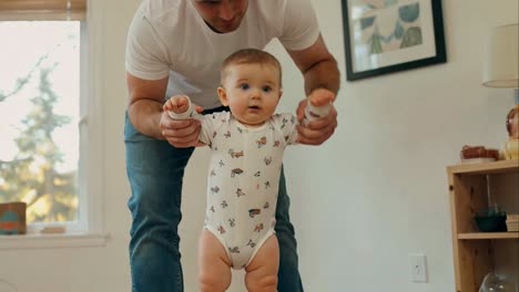 Father Helping Baby Take First Steps Indoors