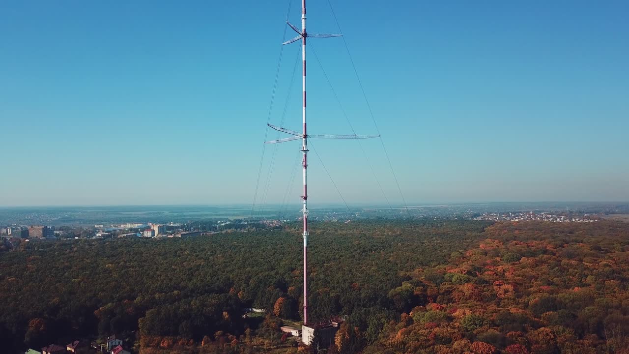 high telecommunication antenna on the background of forest and cityscape. Camera motion up