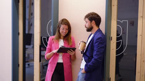 Content-colleagues-standing-in-office-using-tablet