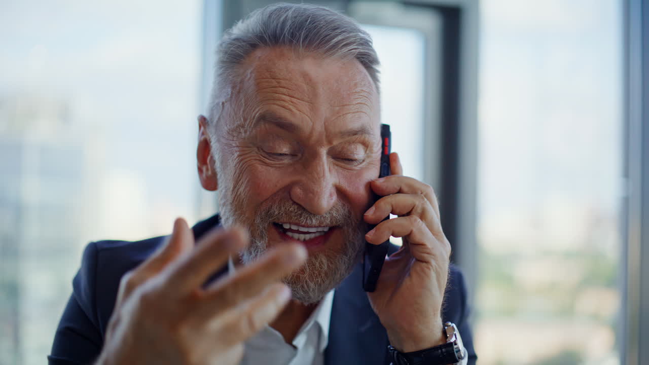 Joyful elderly ceo calling cellphone sharing business success in office closeup