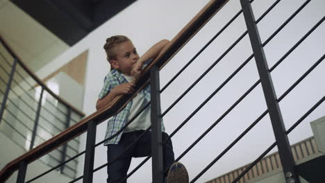 schoolboy leaning stairs railing looking corridor. boy standing stairway alone.