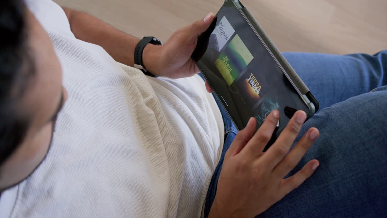 African American man tapping swiping tablet on lap at home with numbers appearing, selecting tiles