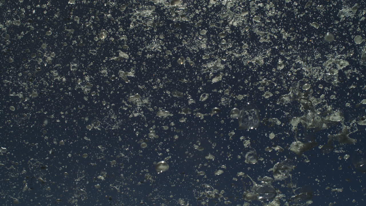 Motion shot of spray particles exploding from ocean in dense misty blast at night