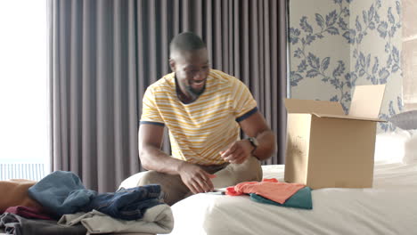 packing clothes into cardboard box, african american man organizing belongings at home