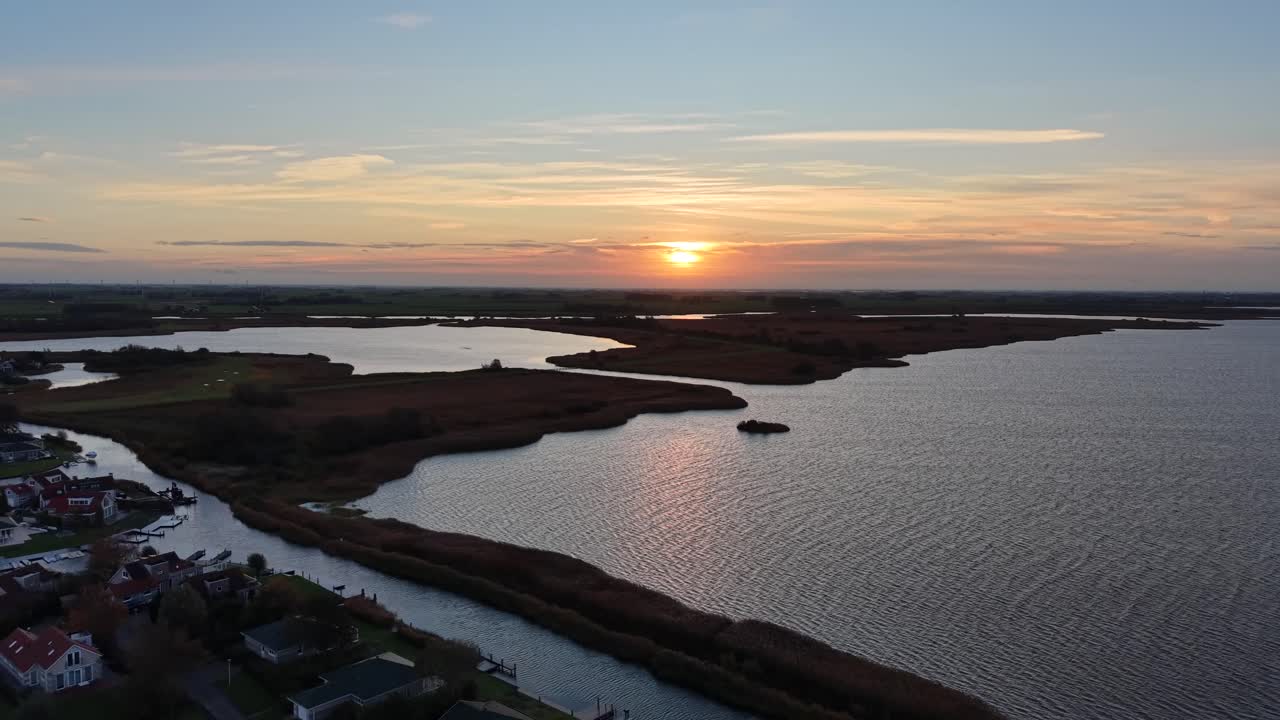 Suave amanecer sobre los humedales holandeses con canales de agua sinuosos, lagos tranquilos y reflectantes, tonos dorados en el cielo y un paisaje amplio y llano. Ambiente apacible de madrugada en Europa. Ascenso con dron, toma amplia