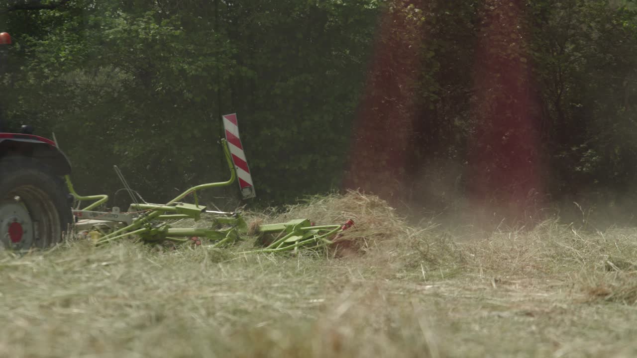 rastrillo de heno rotativo en acción detrás de un tractor rastrillando hierba seca para envasar