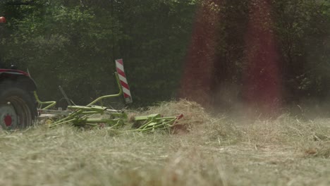 Rastrillo-De-Heno-Giratorio-En-Acción-Detrás-De-Un-Tractor-Rastrillando-Pasto-Seco-Para-Empacar