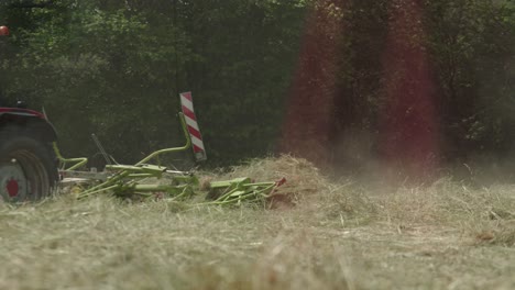 rastrillo de heno rotativo en acción detrás de un tractor rastrillando hierba seca para envasar