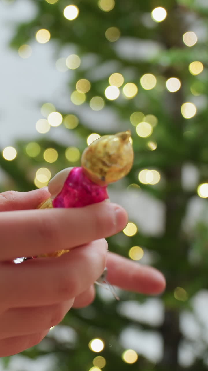 조명 켜진 크리스마스 트리 보케를 배경으로 아이가 천사 장식을 들고 있는 클로즈업 사진이에요. 따뜻한 빛, 섬세한 손길, 휴일의 향수, 가족 전통, 아늑한 인테리어, 금박 유리 장식품을 살펴보고 있어요.