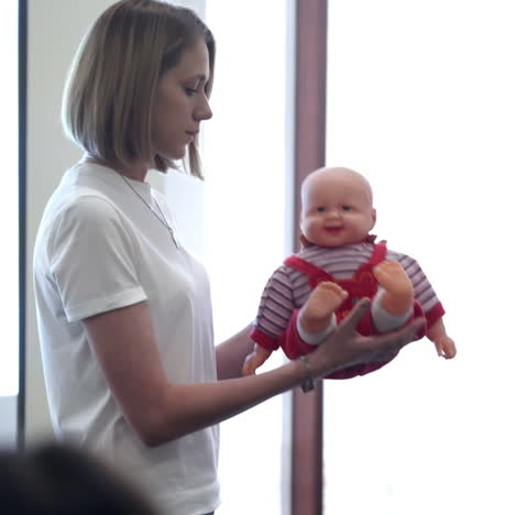 young woman with a doll on public meeting. female lecturer conducts speech holding a doll and explaining how to look after the small kids.