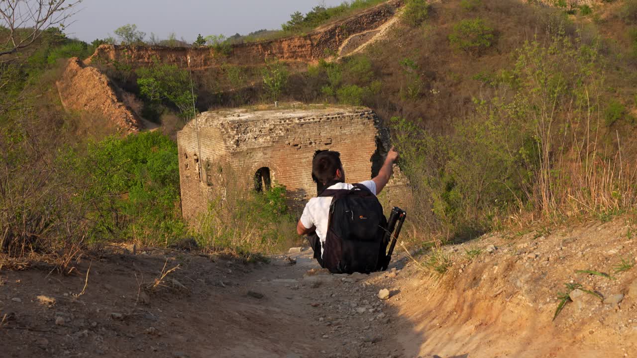 un hombre con una mochila se sienta en un camino polvoriento frente a la torre haowang apuntando a otras torres de la gran muralla, beijing.