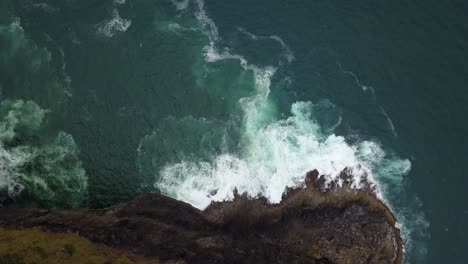 overhead aerial view of waves splashing below cliffs on the oregon coast