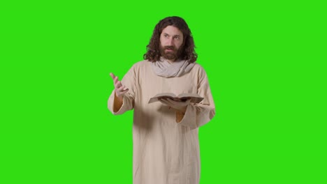 Studio-Shot-Of-Man-Wearing-Robes-With-Long-Hair-And-Beard-Representing-Figure-Of-Jesus-Christ-Preaching-From-Bible-On-Green-Screen-