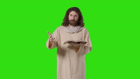 studio shot of man wearing robes with long hair and beard representing figure of jesus christ preaching from bible on green screen