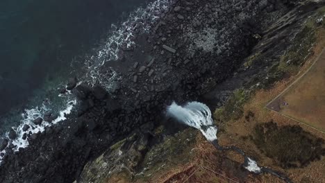 Clear-waterfall-crashing-off-the-rocks-below-at-Kilt-Rock,-Isle-of-Skye,-Aerial-birds-eye-view