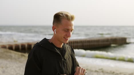 portrait of a young man who listens to music with headphones and walks along the beach in the morning