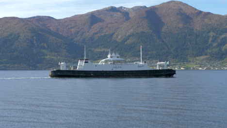 Eine-Norwegische-Fähre-Fährt-An-Einem-Sonnigen-Tag-Durch-Einen-Fjord-Mit-Wunderschönen-Bergen-Im-Hintergrund,-Zeitlupe