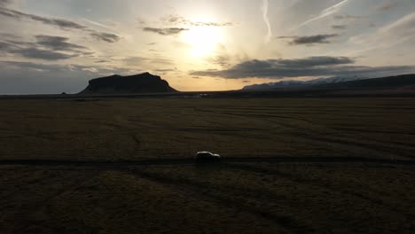 aerial shot of an suv traveling across the vast plains of búrfell, iceland, with the sun setting behind distant mountains and a dramatic sky