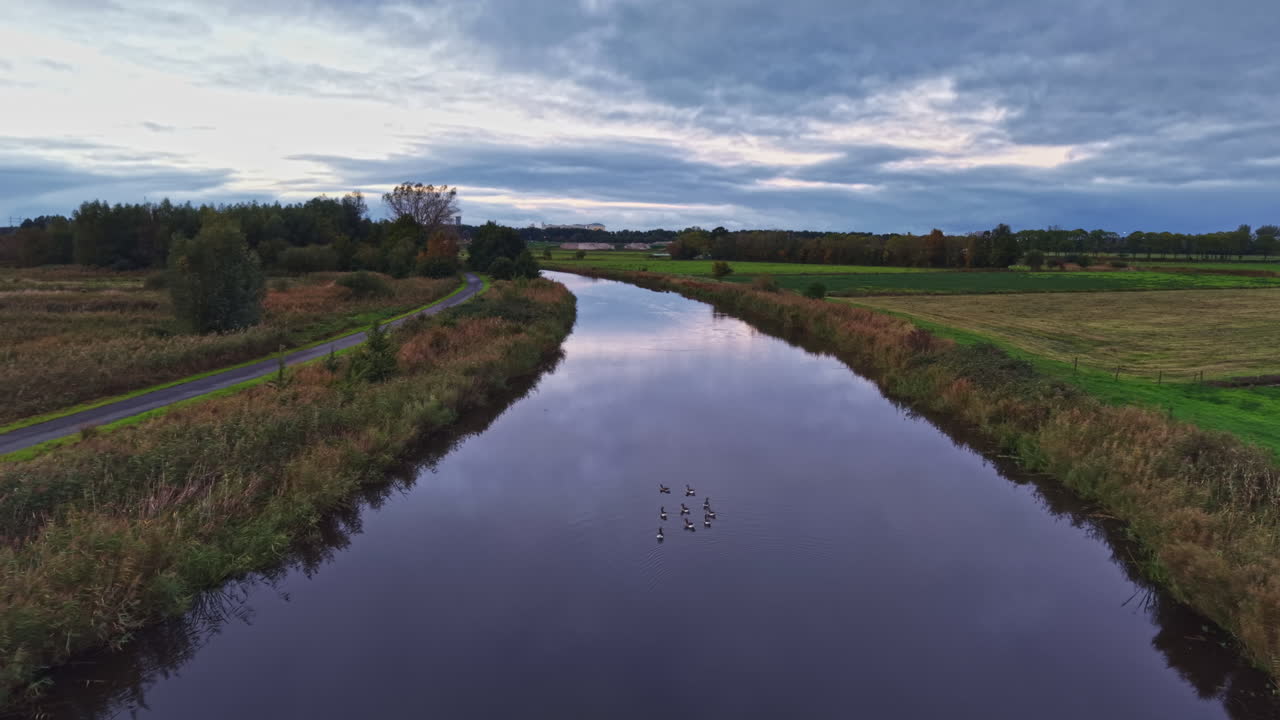 Serene waters reflect the overcast sky near a peaceful countryside path at dusk