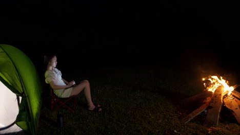 woman-girl-asiatic-chatting-typing-on-tablet-while-in-front-of-bonfire-with-her-camping-tent