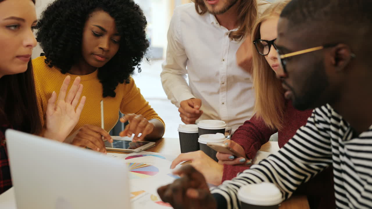 Close-up view of multiethnic coworkers viewing graphics and talking sitting at a table in a cafe
